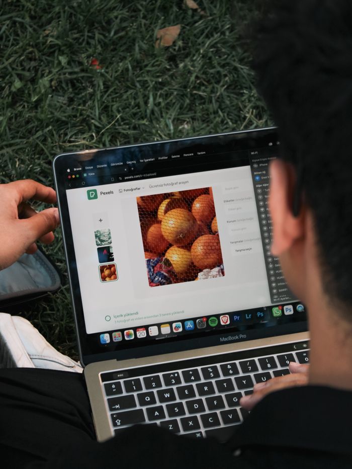creative-03 A man edits a fruit image on a MacBook Pro while sitting outdoors on grass.